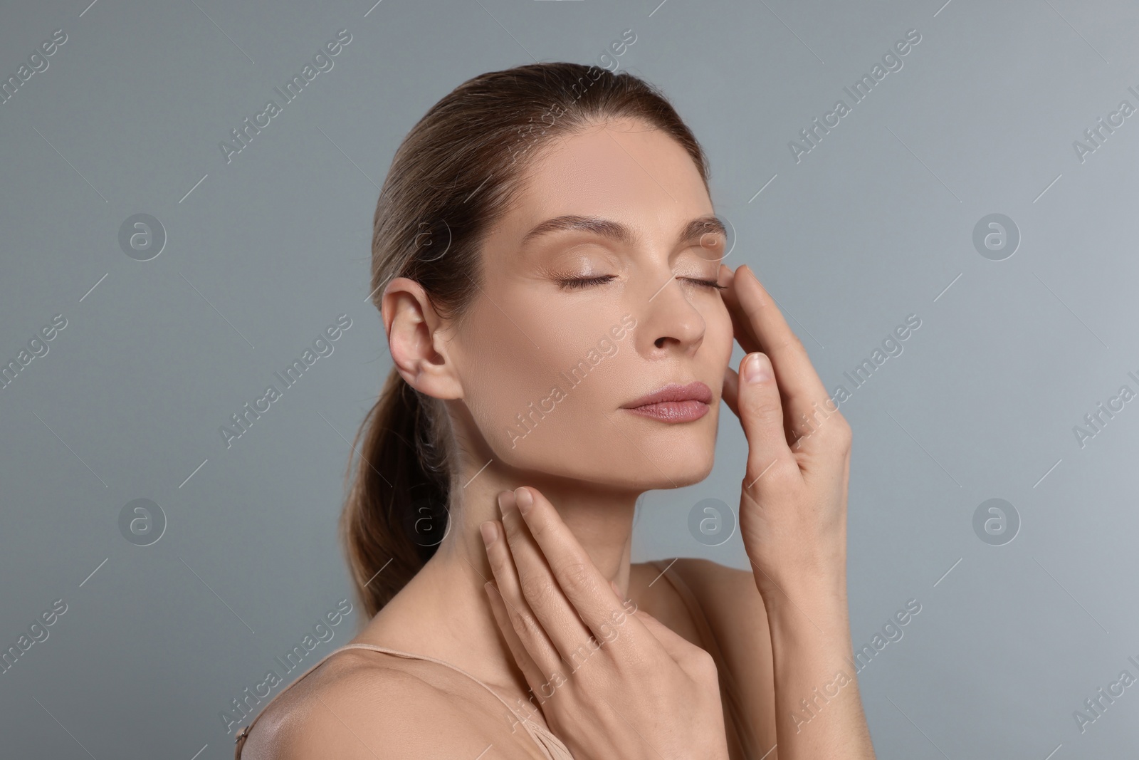 Photo of Woman massaging her face on grey background