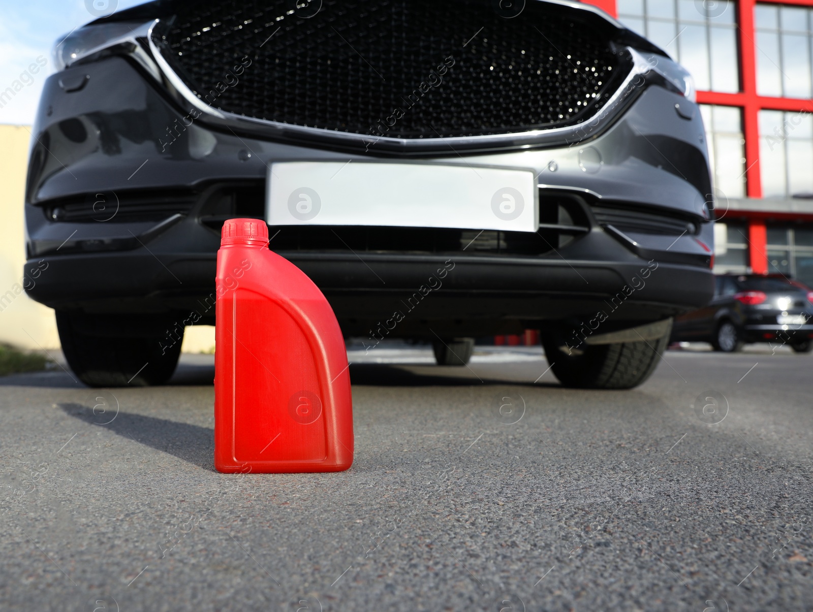 Photo of Red canister with motor oil near car on asphalt road, low angle view