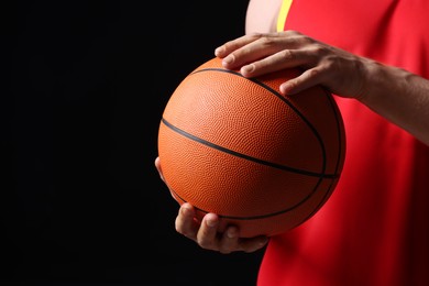 Athletic man with basketball ball on black background, closeup. Space for text