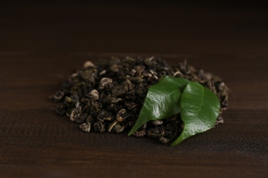 Photo of Heap of dried green tea leaves on wooden table, closeup