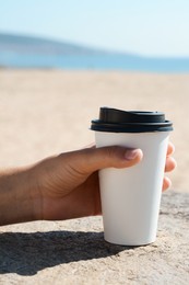 Photo of Woman with takeaway coffee cup on beach, closeup