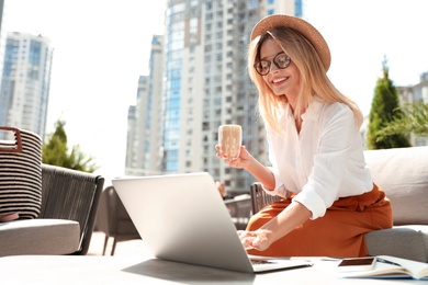 Photo of Beautiful woman with coffee using laptop at outdoor cafe