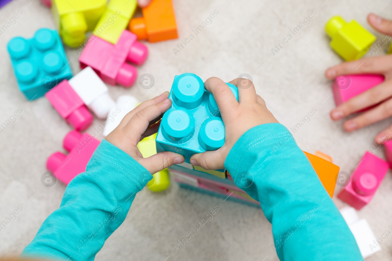 Photo of Top view of little child playing with building blocks on carpet, closeup