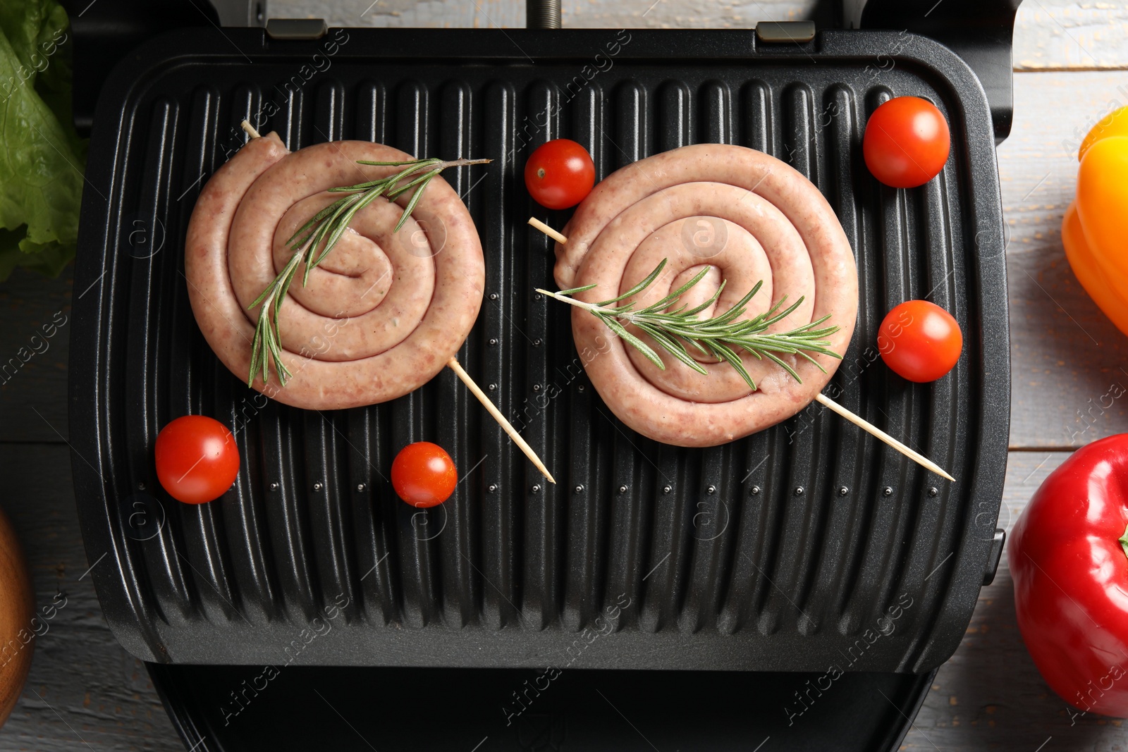 Photo of Electric grill with homemade sausages, rosemary and vegetables on rustic wooden table, flat lay