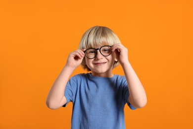 Photo of Cute little boy wearing glasses on orange background