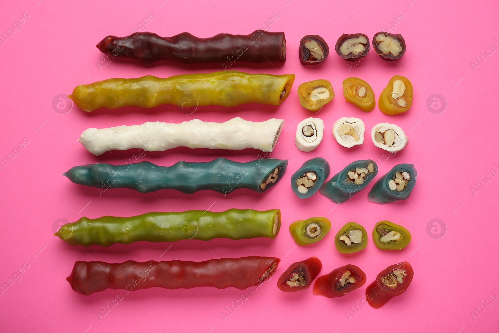 Photo of Many different delicious churchkhelas on pink background, flat lay