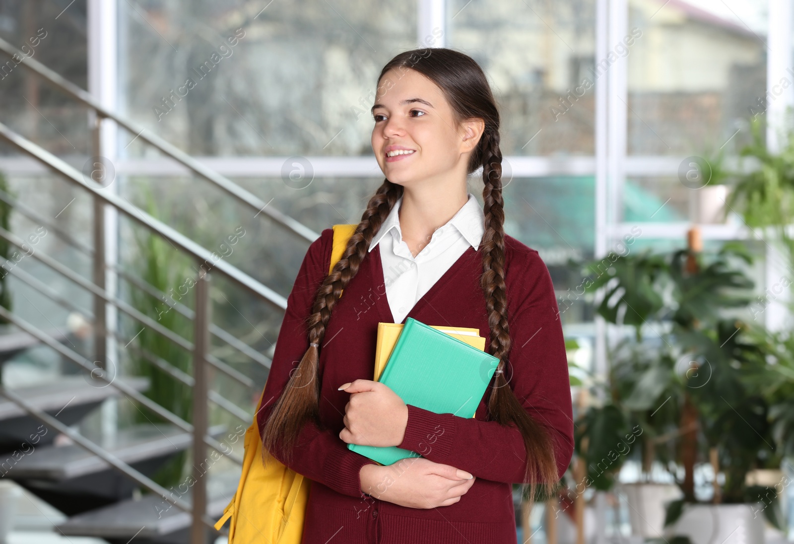 Photo of Teenage girl in school uniform with books and backpack indoors