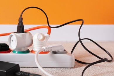 Photo of Power strip with different electrical plugs on white carpet indoors, closeup