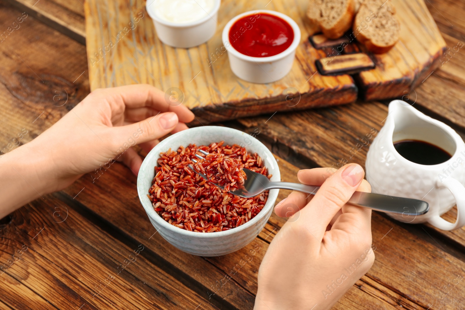 Photo of Woman eating tasty brown rice at wooden table, closeup