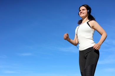 Young woman listening to music while running outdoors in morning, low angle view. Space for text