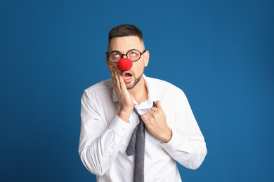 Photo of Funny man with glasses and clown nose on blue background. April fool's day