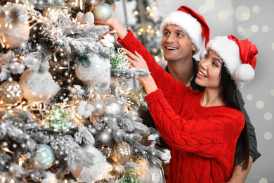 Image of Happy young couple in Santa hats decorating Christmas tree together at home
