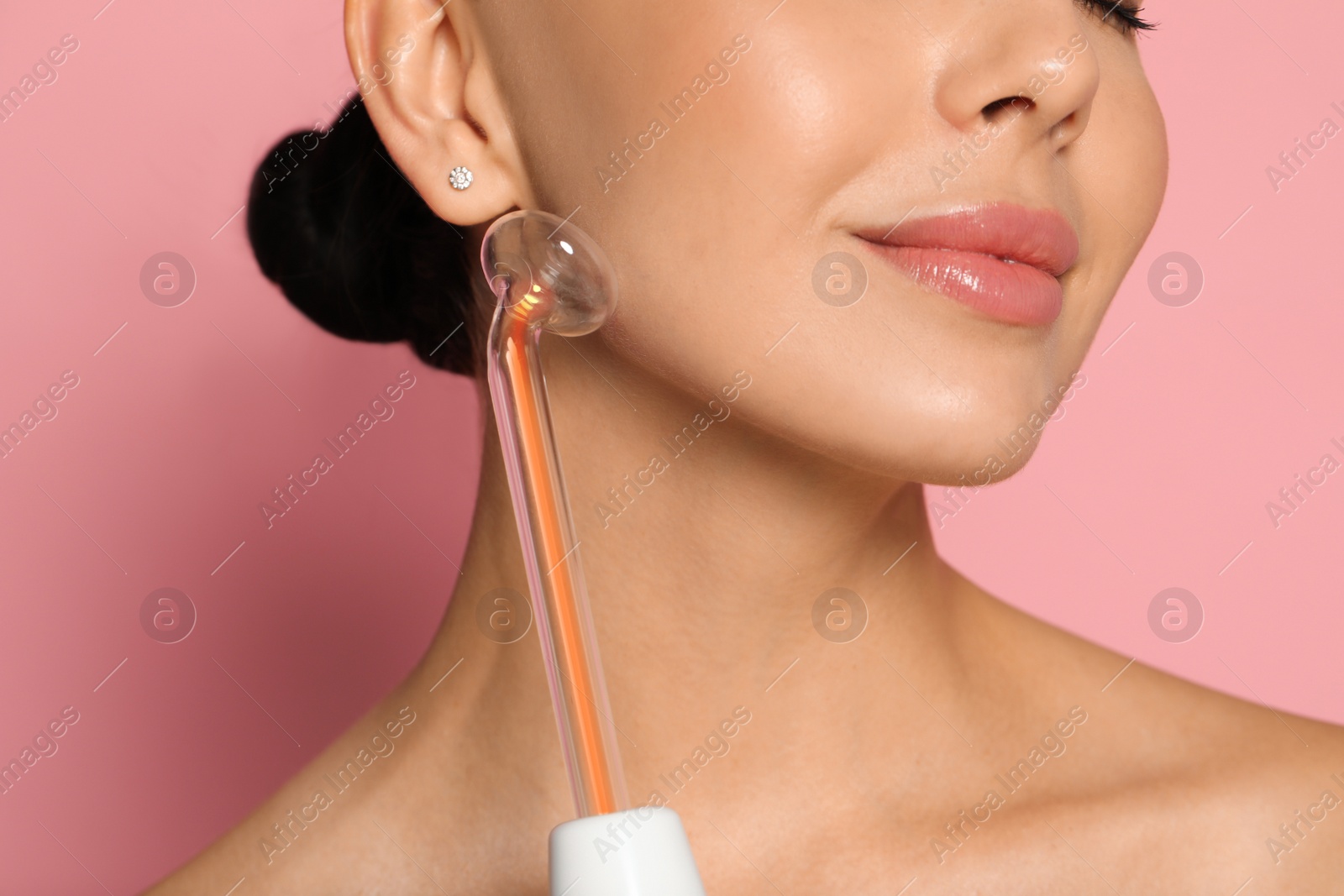 Photo of Woman using high frequency darsonval device on pink background, closeup