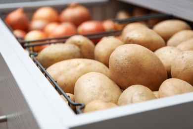 Photo of Open drawer with potatoes and onions, closeup. Orderly storage