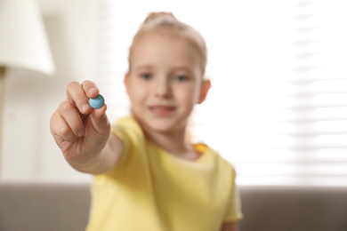 Photo of Little girl with vitamin pill at home, focus on hand