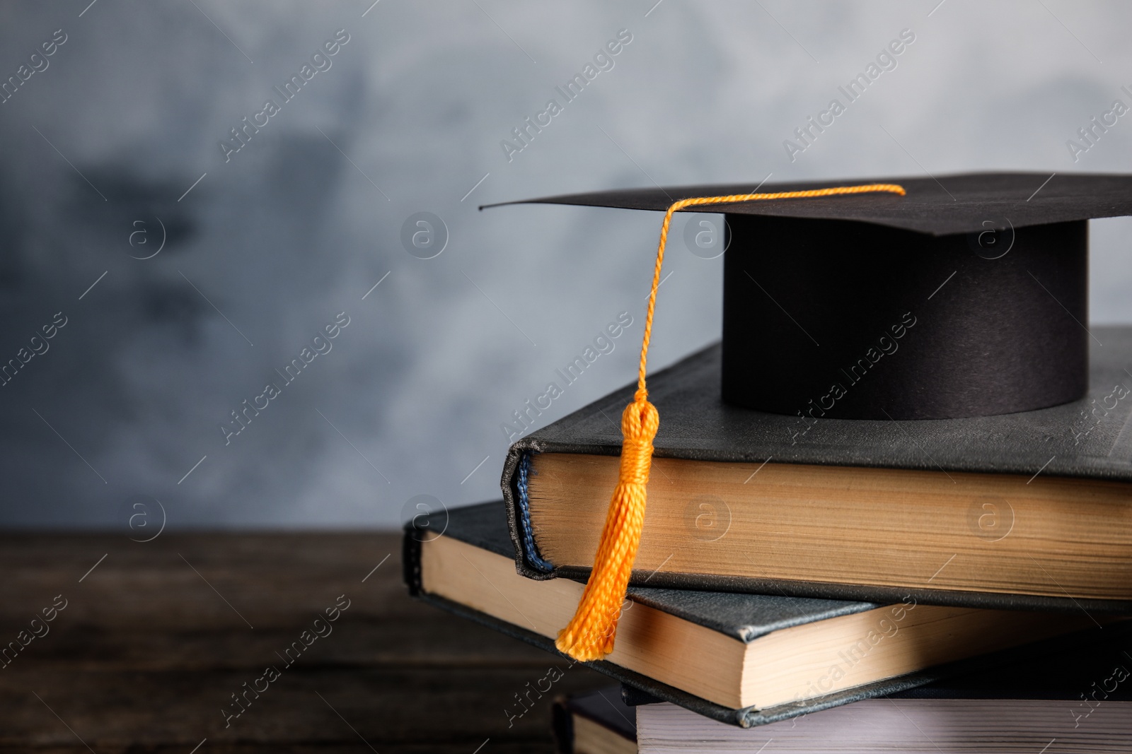 Photo of Graduation hat, books and student's diploma on wooden table against light blue background