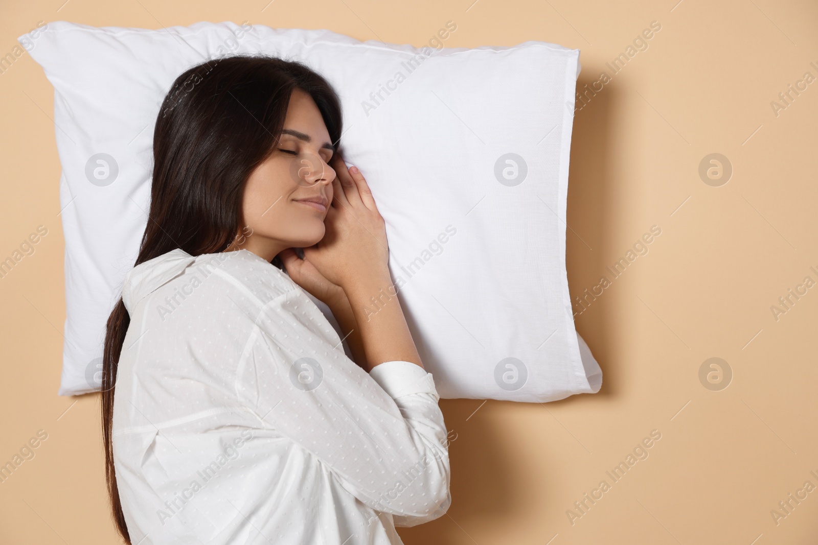 Photo of Young woman sleeping on soft pillow against beige background