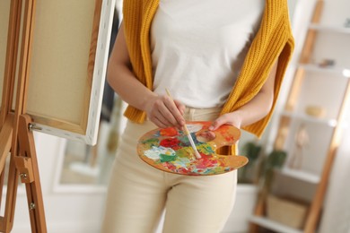 Photo of Young woman drawing on easel at home, closeup