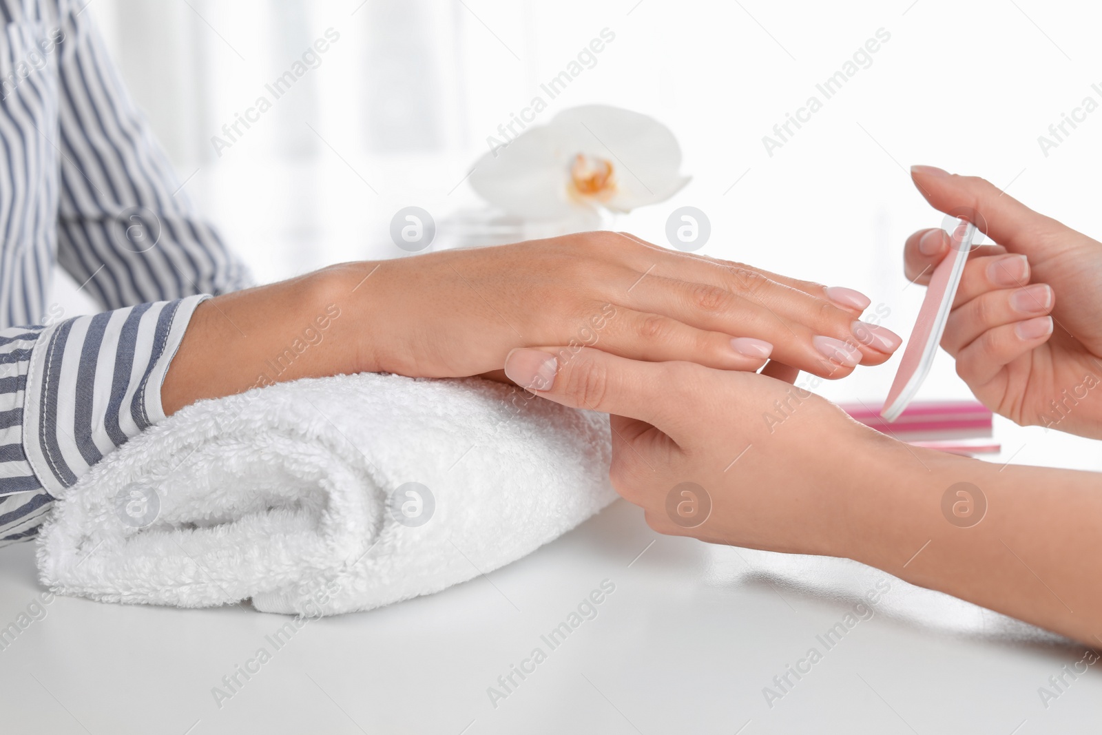 Photo of Manicurist filing client's nails covered with polish in salon, closeup