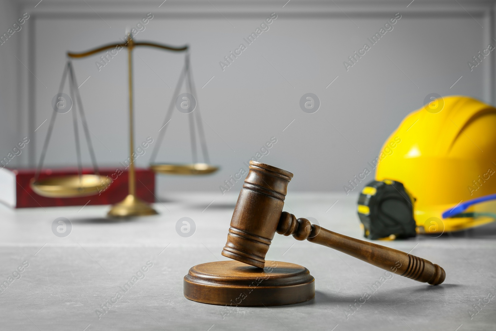 Photo of Construction and land law concepts. Judge gavel, scales of justice, tape measure with hardhat on light grey table