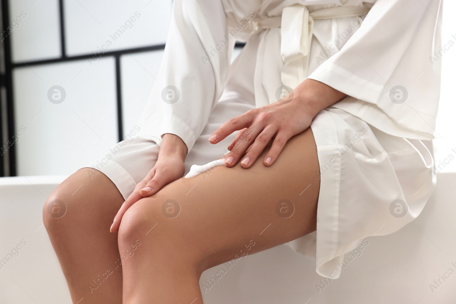 Photo of Woman applying self-tanning product onto her leg on tub in bathroom, closeup