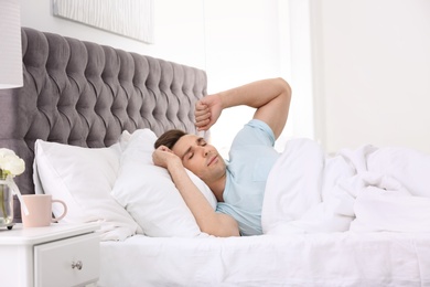 Photo of Young man waking up in bed with pillows at home