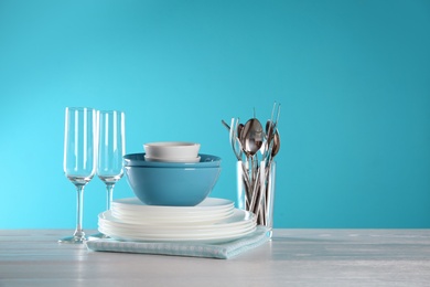 Set of clean dishes, glasses and cutlery on table against color background