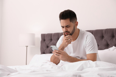 Young man addicted to smartphone in bed at home