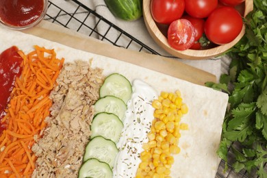 Photo of Delicious tortilla with tuna, vegetables and sauces on wooden table, flat lay. Cooking shawarma