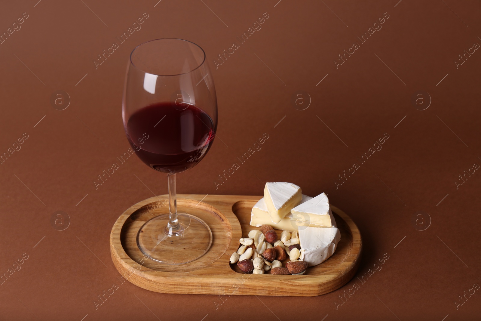 Photo of Glass of red wine, cheese and nuts on brown background, space for text