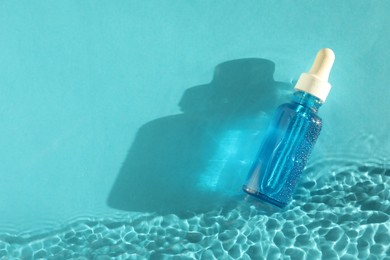 Bottle of cosmetic serum in water on turquoise background, top view. Space for text