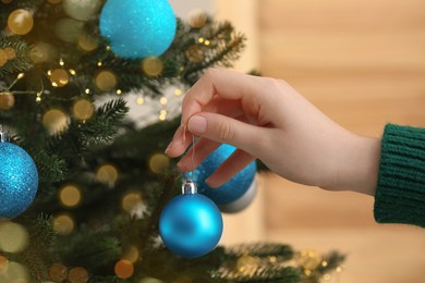 Photo of Woman decorating Christmas tree with beautiful bauble indoors, closeup