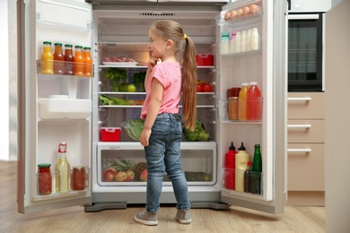 Cute little girl choosing food in refrigerator at home