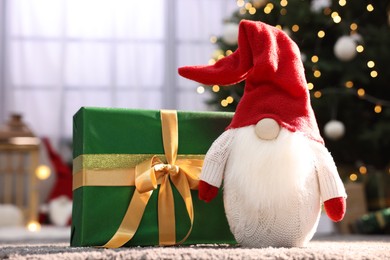 Photo of Beautiful gift box and Christmas gnome on carpet indoors