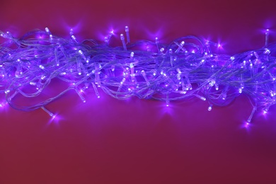 Glowing Christmas lights on burgundy background, space for text