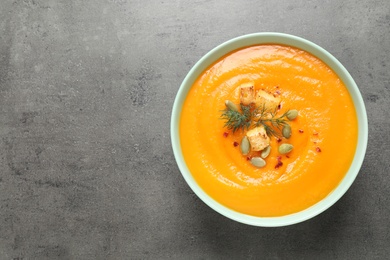 Photo of Delicious pumpkin soup in bowl on grey table, top view. Space for text