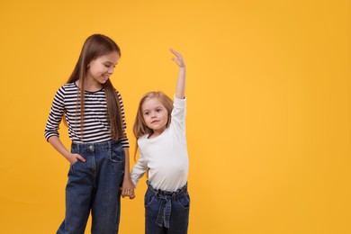Photo of Portrait of cute little sisters on orange background, space for text