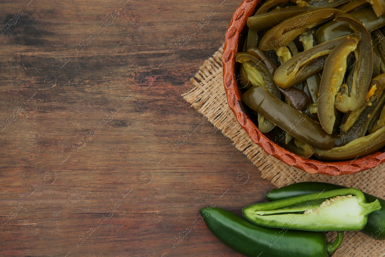 Photo of Fresh and pickled green jalapeno peppers on wooden table, flat lay