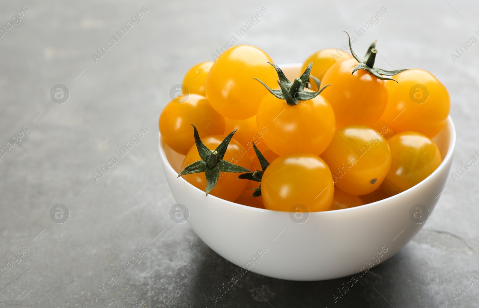 Photo of Ripe yellow tomatoes on grey table. Space for text