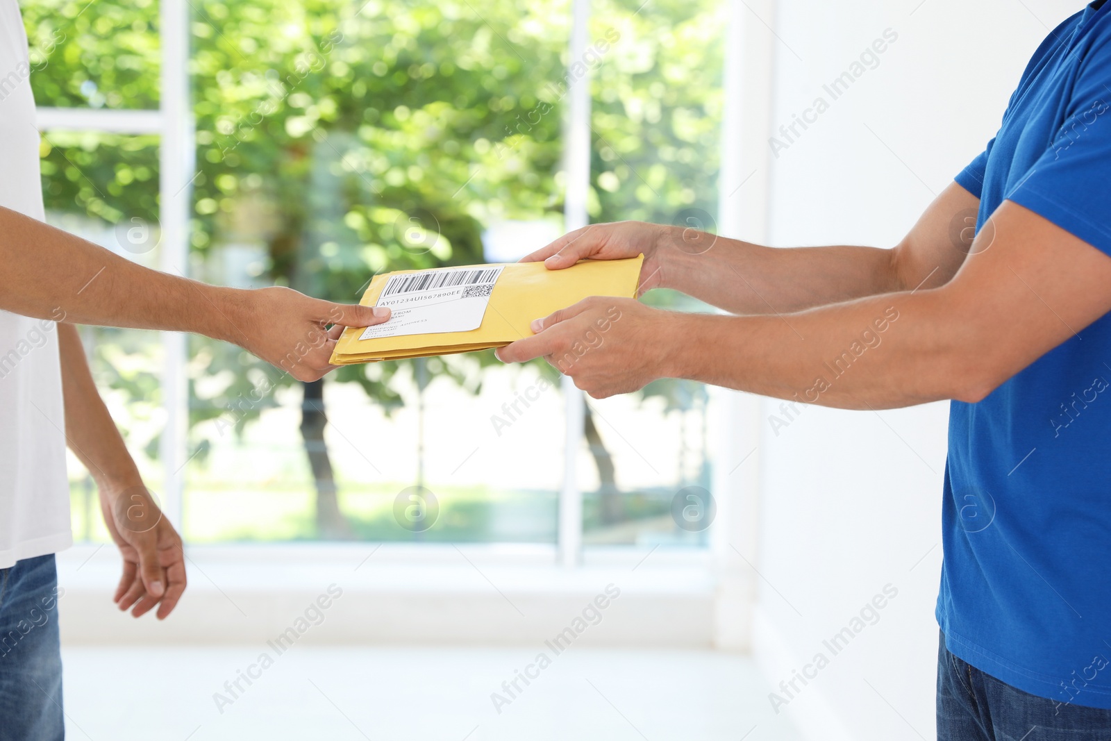 Photo of Young courier giving envelopes to client near window indoors, closeup