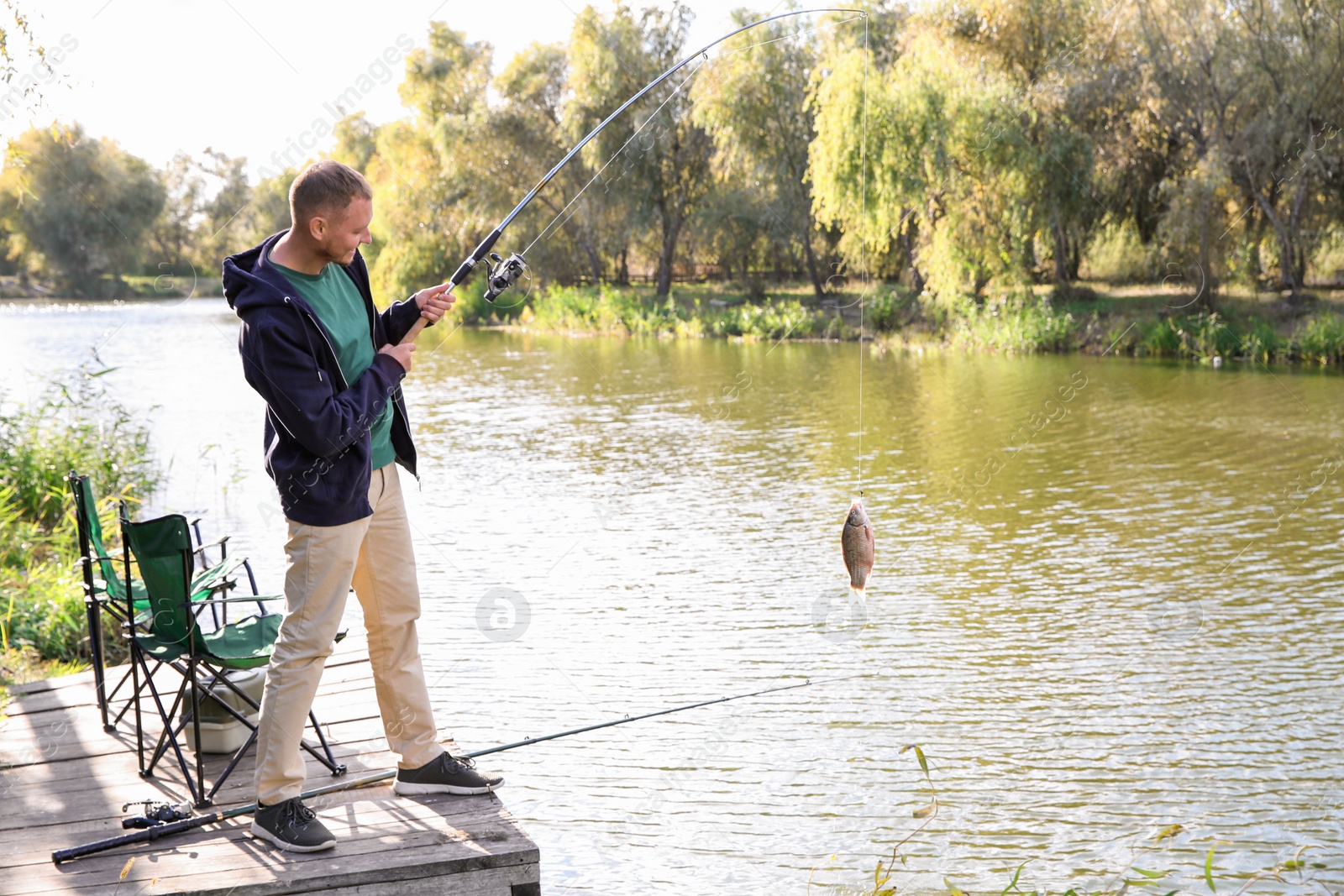 Photo of Man with rod fishing on wooden pier at riverside. Recreational activity