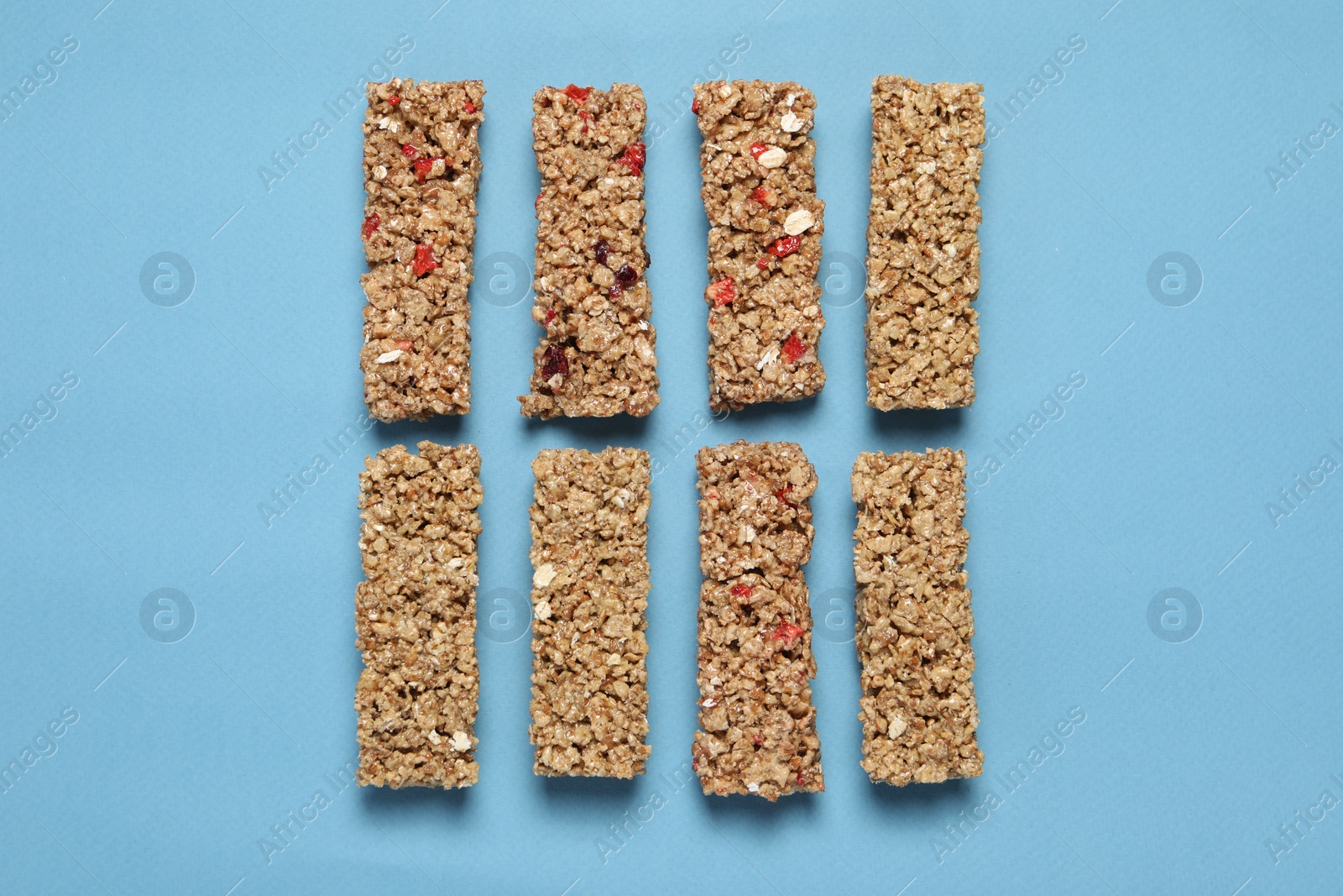 Photo of Different tasty granola bars on light blue background, flat lay