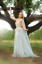 Photo of Beautiful girl wearing fairy dress near tall tree outdoors