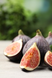 Whole and cut ripe figs on light wooden table against blurred green background, closeup