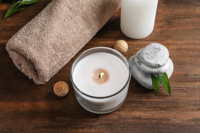 Photo of Beautiful composition with spa stones, towel and burning candle on wooden table