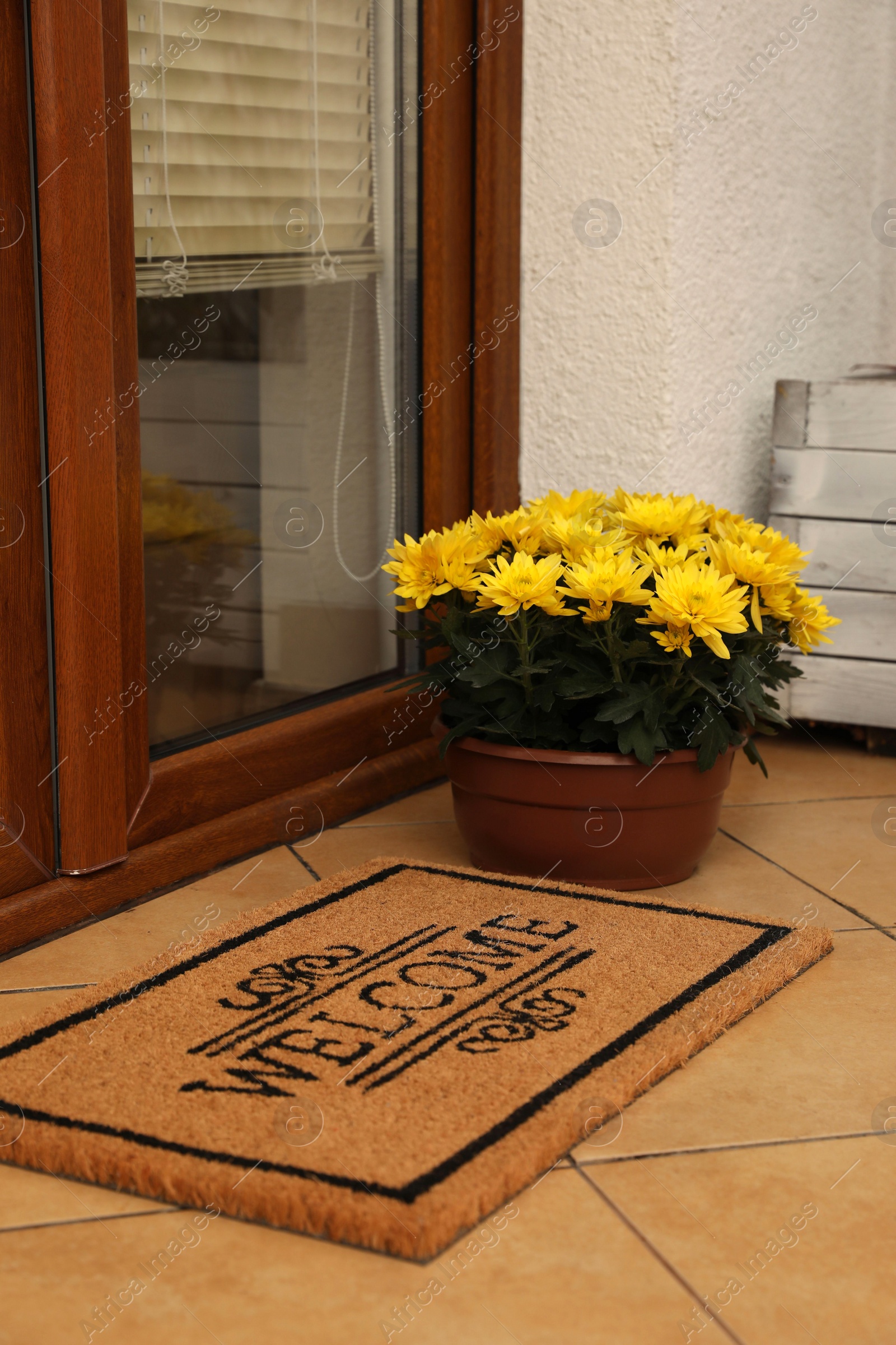 Photo of Door mat with word Welcome and beautiful flowers on floor near entrance