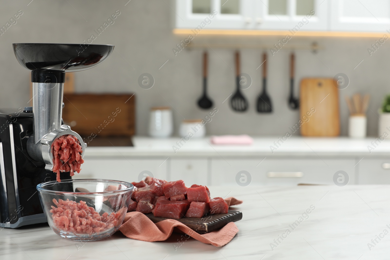 Photo of Electric meat grinder with beef mince on white table in kitchen, space for text