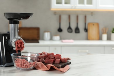 Electric meat grinder with beef mince on white table in kitchen, space for text