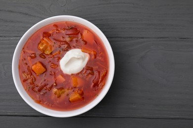 Photo of Tasty borscht with sour cream on grey wooden table, top view. Space for text