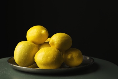 Plate with whole lemons on small table against dark background